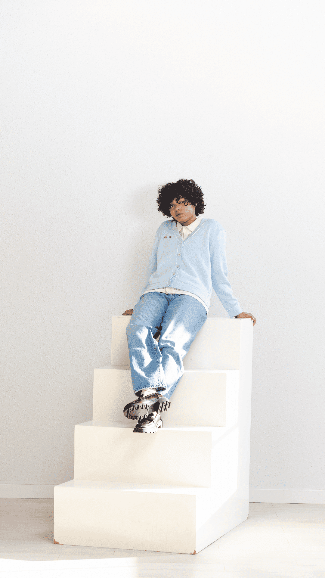 Person in light blue cardigan and jeans sitting on white stepped platform.