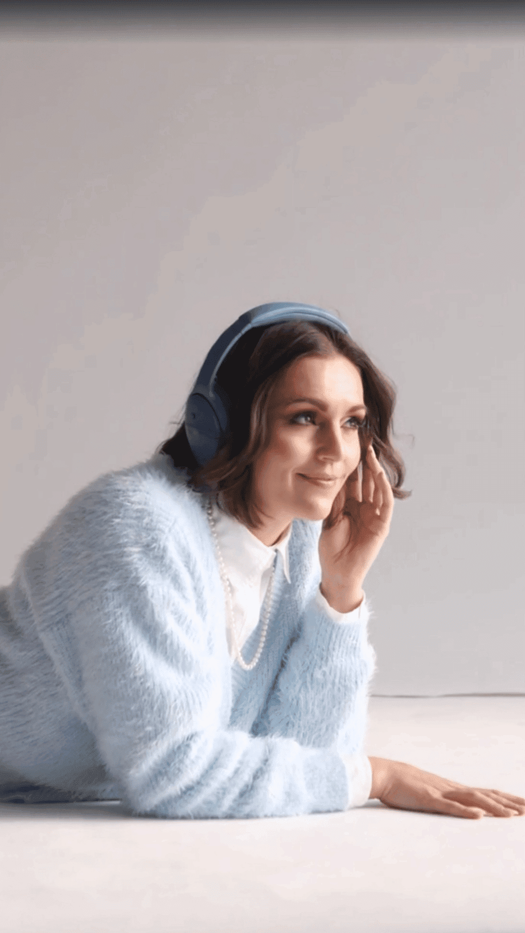 Woman in blue sweater and headphones listening intently.